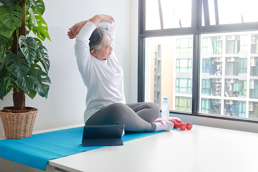 Asian elderly women exercise home arm stretches according trainer tablet