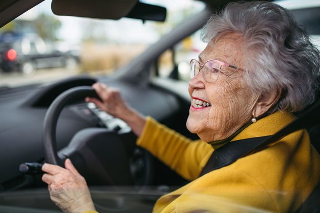 Happy senior woman driving car alone enjoying car ride safe