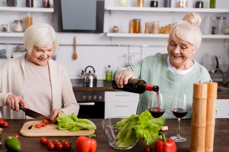 happy senior woman pouring red wine glass retired friend cutting happy senior woman pouring red wine glass retired friend cutting