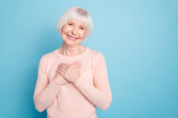 Portrait of positive woman putting her palm on chest smiling wearing pastel sweater isolated over blue background Portrait of positive woman putting her palm on chest smiling wearing pastel sweater isolated over blue background
