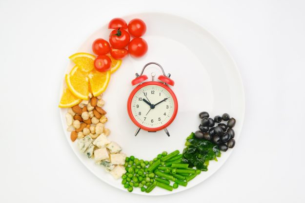 Diet and lunchtime, Intermittent fasting concept. Vegetables, oranges, cheese, nuts and clock on a white plate. Healthy dietary food. Diet and lunchtime, Intermittent fasting concept. Vegetables, oranges, cheese, nuts and clock on a white plate. Healthy dietary food.