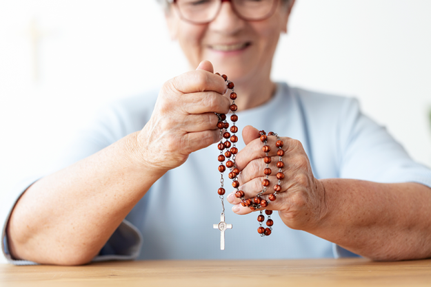 Close smiling elderly person holding rosary cross focus hands