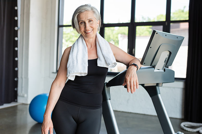 Happy senior woman white towel shoulders standing next treadmill Happy senior woman white towel shoulders standing next treadmill