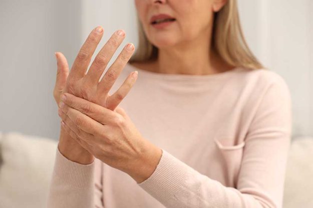 Mature woman suffering pain hand indoors closeup rheumatism symptom
