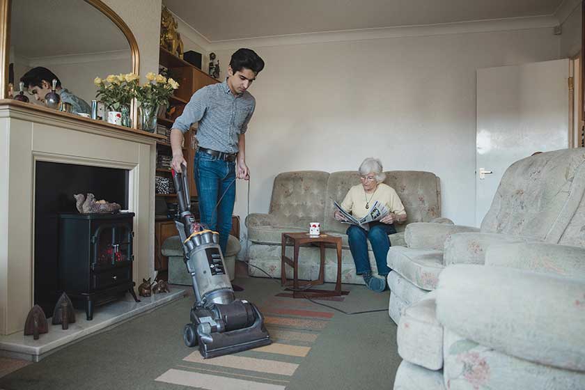 teenage boy hoovering his grandmother living room her while she Teenage boy hoovering his grandmother living room her while she