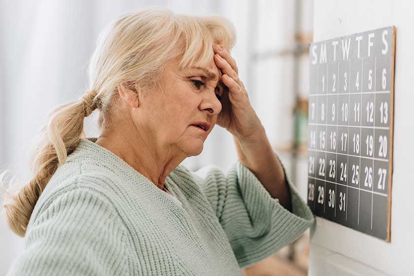 Upset woman gray hair touching head looking wall calendar