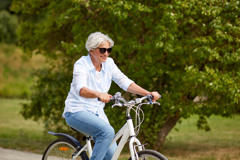 happy senior woman riding bicycle at summer park