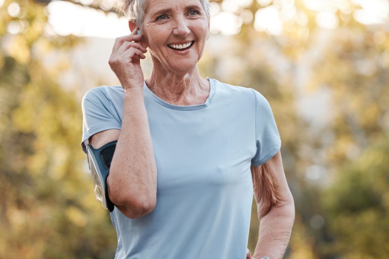 Senior woman, run outdoor and happy with music or audio podcast for lifestyle motivation, runner fitness and exercise workout. Elderly athlete, smile and training or running rest in nature park