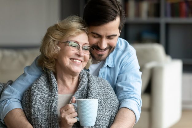 Young man cuddling wrapped in plaid smiling 60s elderly mother.