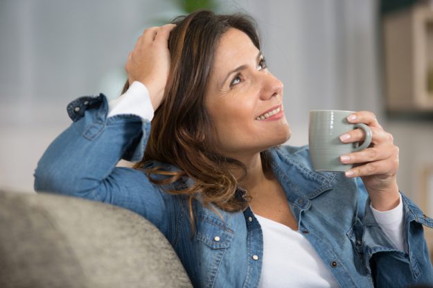 smiling woman sitting on sofa while drinking tea smiling woman sitting on sofa while drinking tea