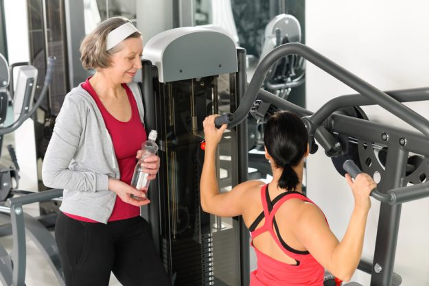 Personal trainer at fitness center showing exercise to senior woman Personal trainer at fitness center showing exercise to senior woman