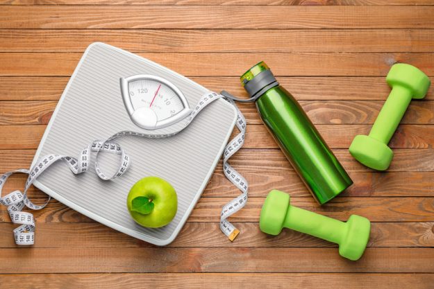 Weight scales with measuring tape, apple, bottle of water and dumbbells on wooden background Weight scales with measuring tape, apple, bottle of water and dumbbells on wooden background