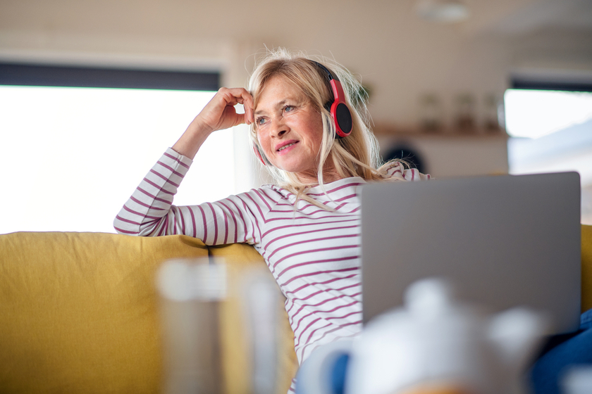 Senior woman with headphones and laptop indoors in home office, relaxing. Senior woman with headphones and laptop indoors in home office, relaxing.