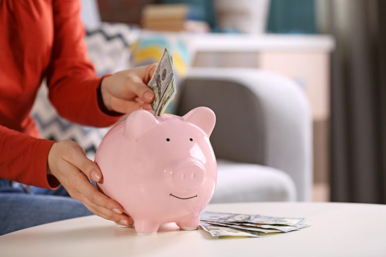 Female hand putting money into piggy bank closeup Female hand putting money into piggy bank closeup