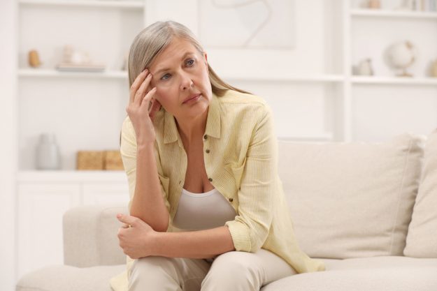 Menopause. Woman suffering from headache on sofa at home