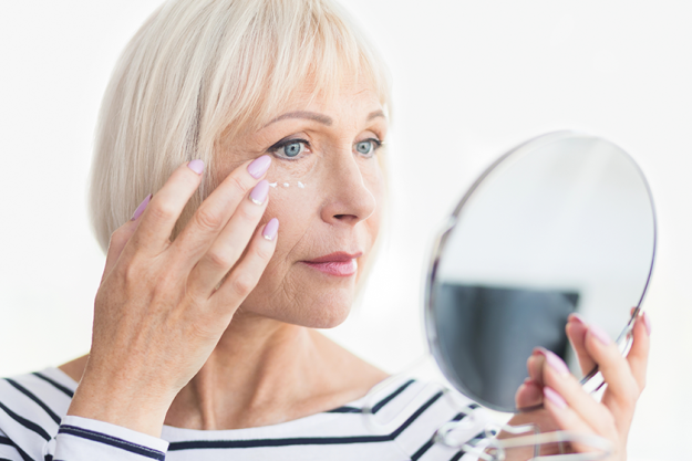 Beautiful elderly woman holding mirror and applying face cream Beautiful elderly woman holding mirror and applying face cream