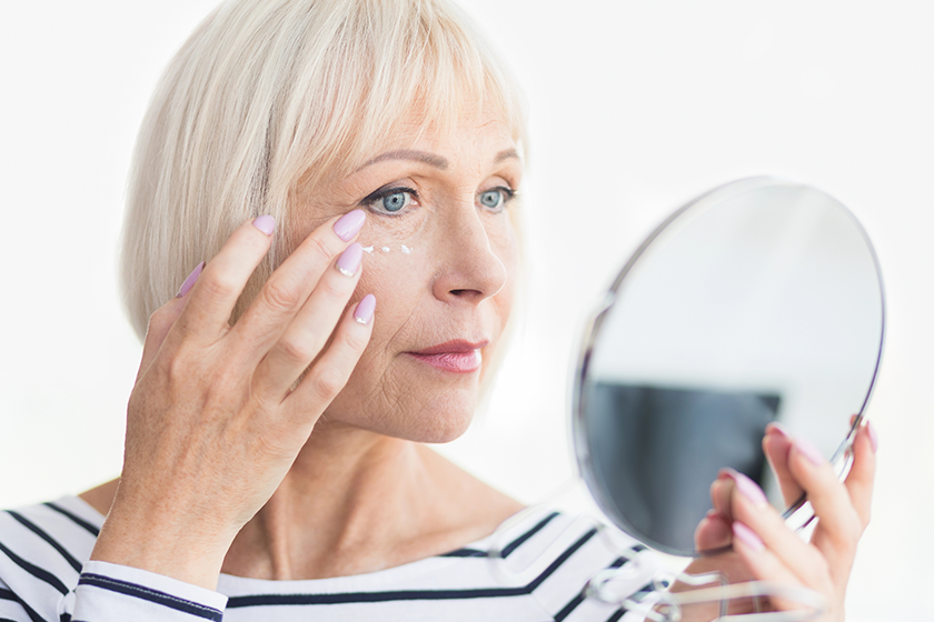 Beautiful elderly woman holding mirror and applying face cream