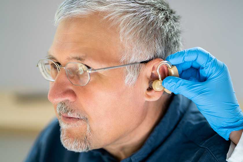 Close doctor putting hearing aid senior patient ear Close doctor putting hearing aid senior patient ear