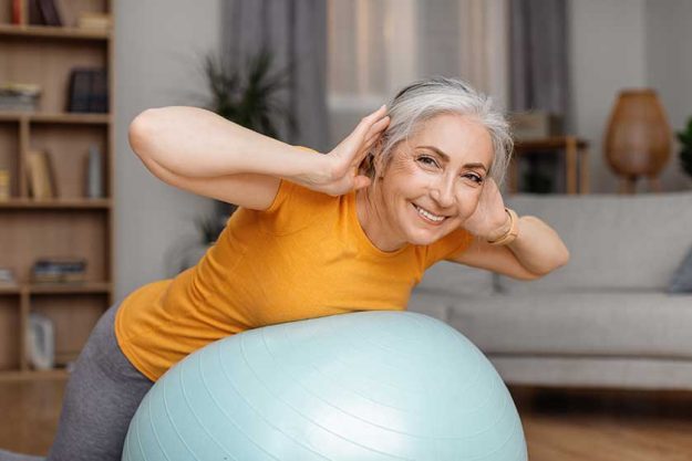 Happy senior woman doing exercises fitness ball home training her