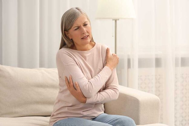 Mature woman suffering pain arm sofa home rheumatism symptom Mature woman suffering pain arm sofa home rheumatism symptom
