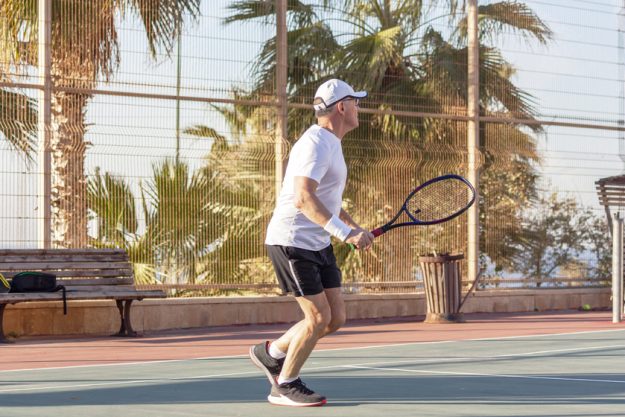 An elderly man plays tennis on an outdoor court