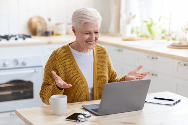 Cheerful senior woman having online class, talking to teacher