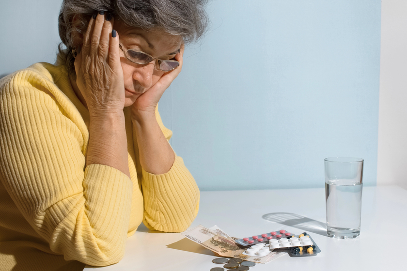 Elderly woman with glasses looking at money and pills on the table. Concept of depression, drug price, treatment cost Elderly woman with glasses looking at money and pills on the table. Concept of depression, drug price, treatment cost