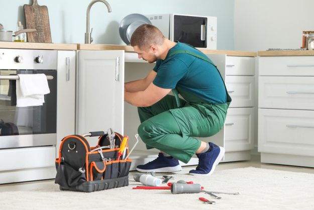 Handsome plumber repairing sink in kitchen Handsome plumber repairing sink in kitchen