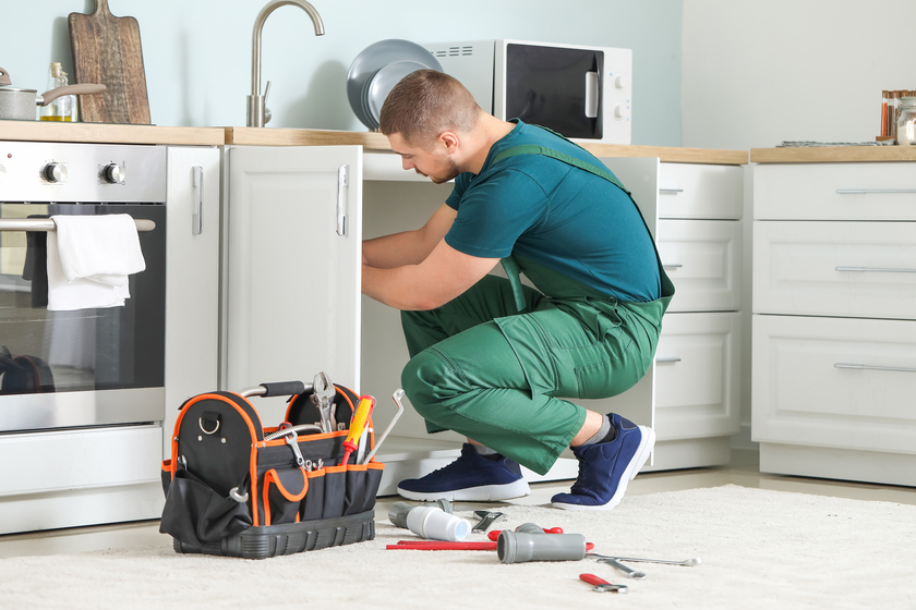 Handsome plumber repairing sink in kitchen