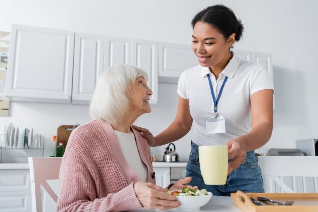 Happy multiracial social worker serving lunch to senior women in grey hair Happy multiracial social worker serving lunch to senior women in grey hair