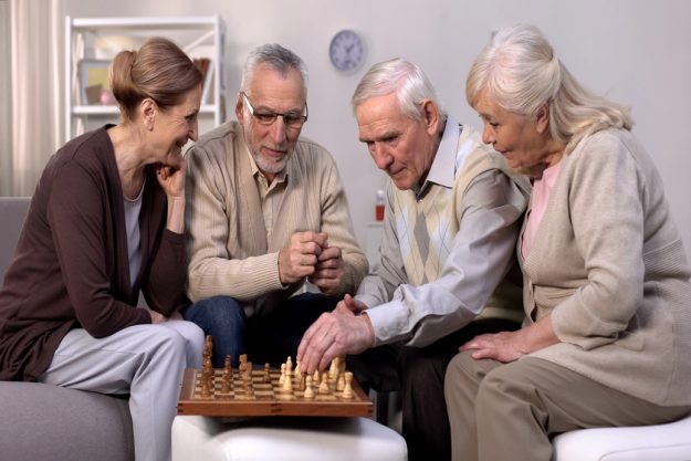 Senior friends playing chess at home, retirement leisure time, togetherness