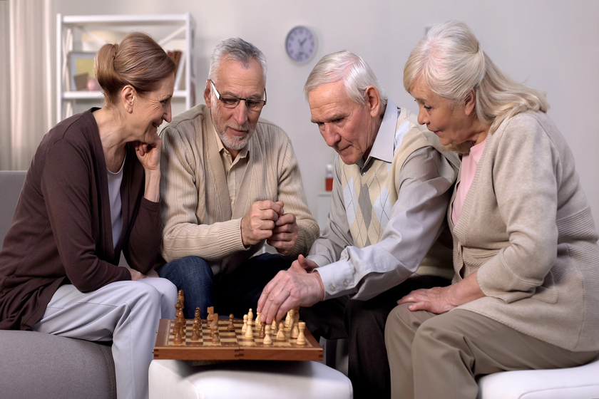 Senior friends playing chess at home, retirement leisure time, togetherness