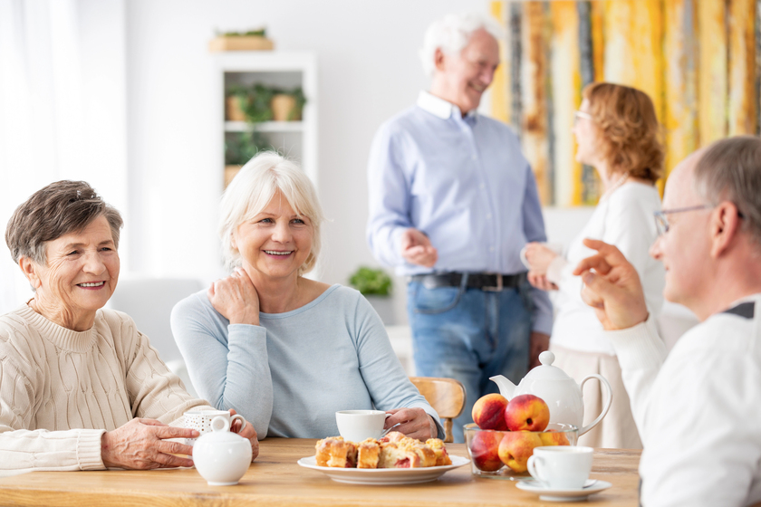 Senior people visiting old friends at home sitting together at wooden table chatting, drinking tea and eating Senior people visiting old friends at home sitting together at wooden table chatting, drinking tea and eating