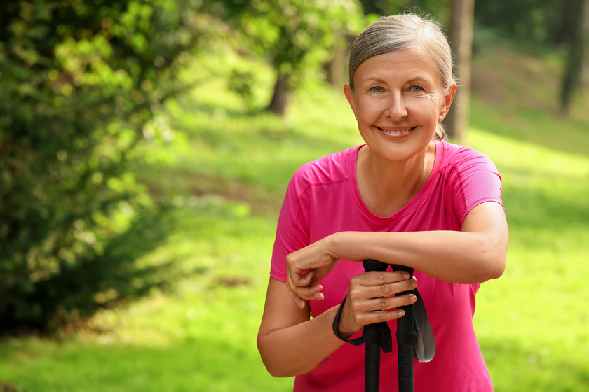 Senior woman with Nordic walking poles outdoors, space for text