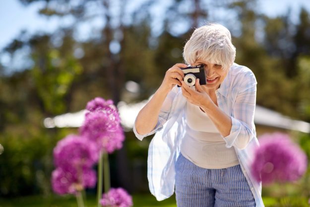 Senior woman with camera photographing flowers — Photo