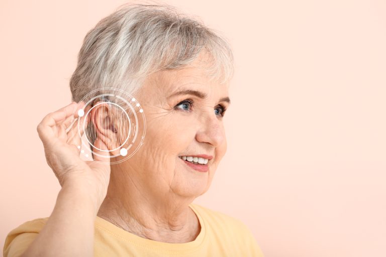 Senior woman with hearing aid on color background