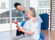 Happy female trainer looking at senior woman lifting dumbbells in gym