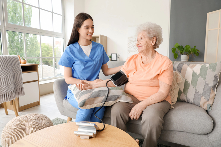 Young nurse measuring senior woman's blood pressure at home
