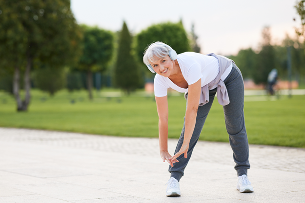 Elderly fit smiling woman wireless headphones doing stretching exercises jogging Elderly fit smiling woman wireless headphones doing stretching exercises jogging