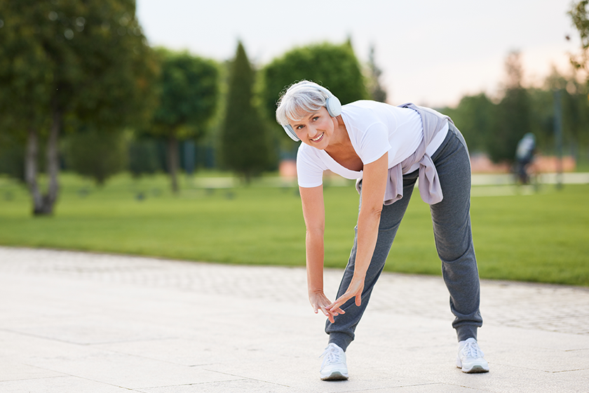 Elderly fit smiling woman wireless headphones doing stretching exercises jogging Elderly fit smiling woman wireless headphones doing stretching exercises jogging