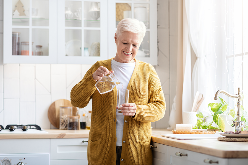 Senior woman pouring water into glass kitchen interior Senior woman pouring water into glass kitchen interior