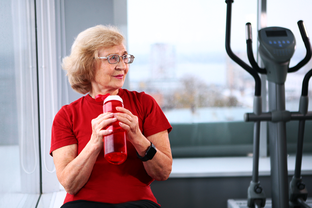 an elderly woman holds a water bottle in the gym