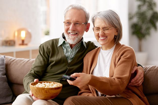 Beautiful happy senior couple husband wife eating popcorn watching while