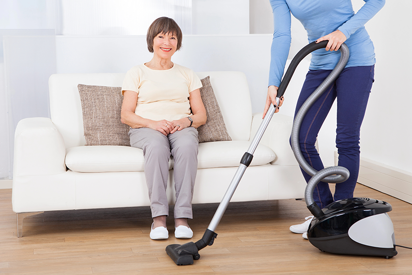 caretaker cleaning floor while senior woman sitting on sofa caretaker cleaning floor while senior woman sitting on sofa