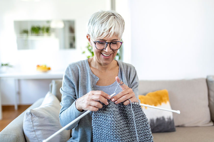 Elderly woman glasses sit couch home smile holding knitting needles