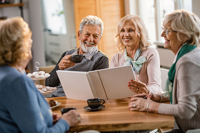 Group happy senior people communicating while looking photo album coffee