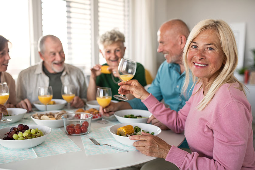 Group of senior friends having party indoors talking when eating at the table