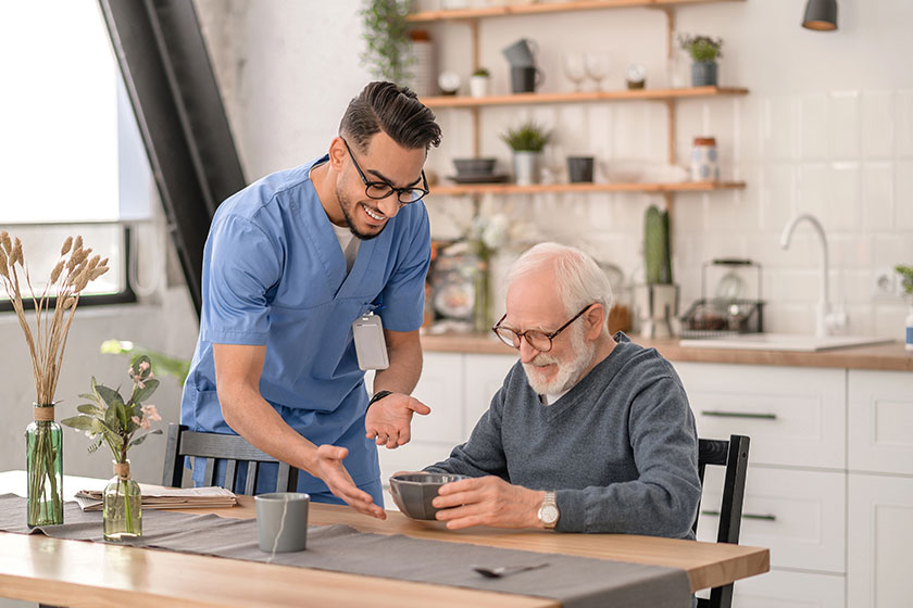 Joyous amiable volunteer serving the meal to an aged man Joyous amiable volunteer serving the meal to an aged man