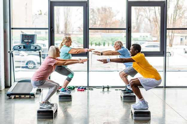 Multicultural senior athletes synchronous doing squats step platforms gym Multicultural senior athletes synchronous doing squats step platforms gym