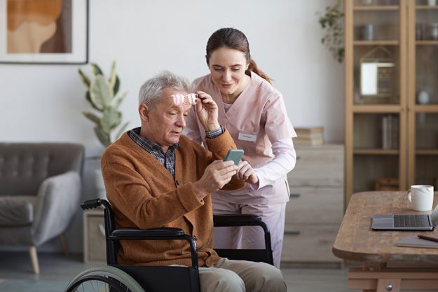 Portrait senior man wheelchair using smartphone caregiver helping him retirement
